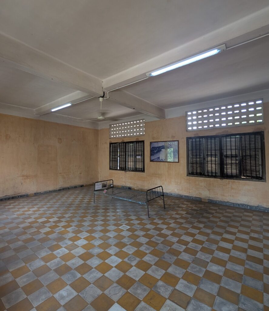 A large, depressing empty room, with a metal bed frame in the middle. 