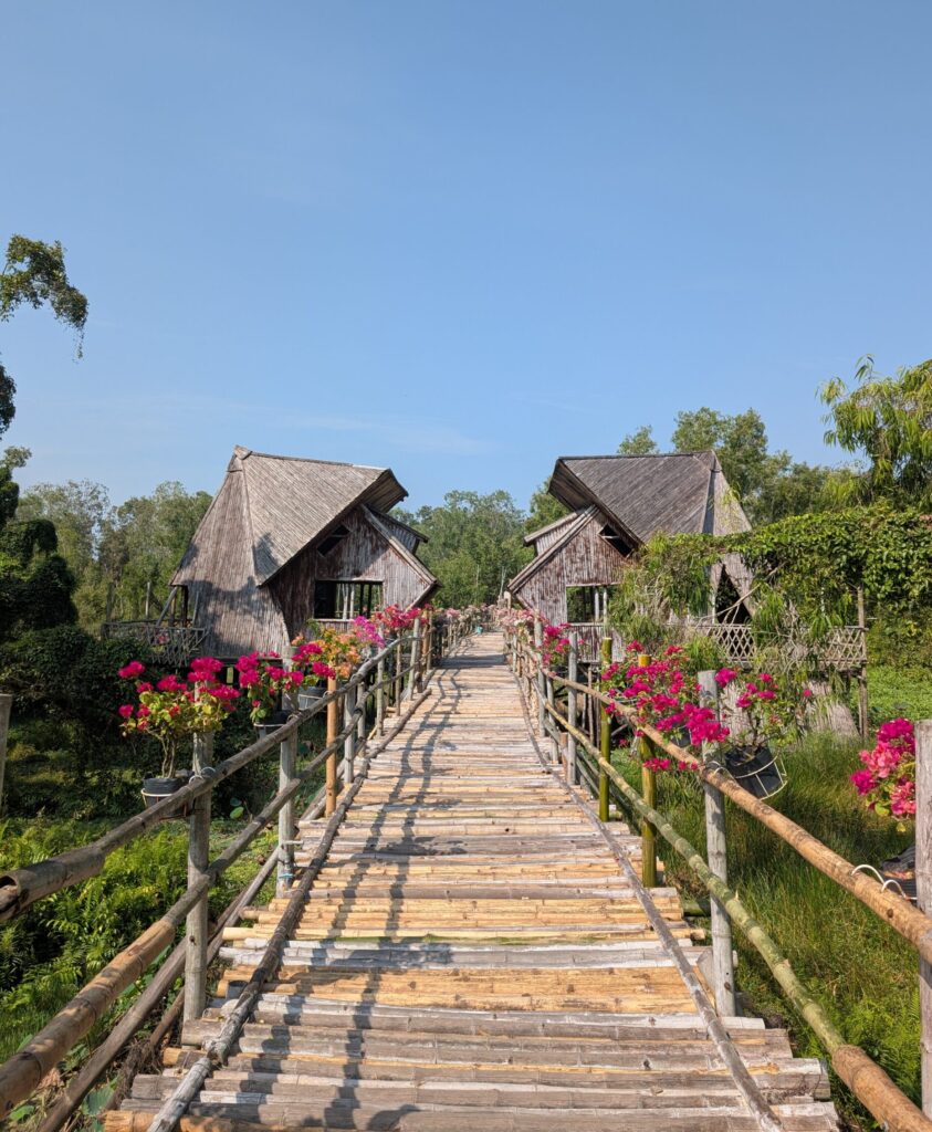 A boardwalk surrounded with pink flowers and wooden bird hides.