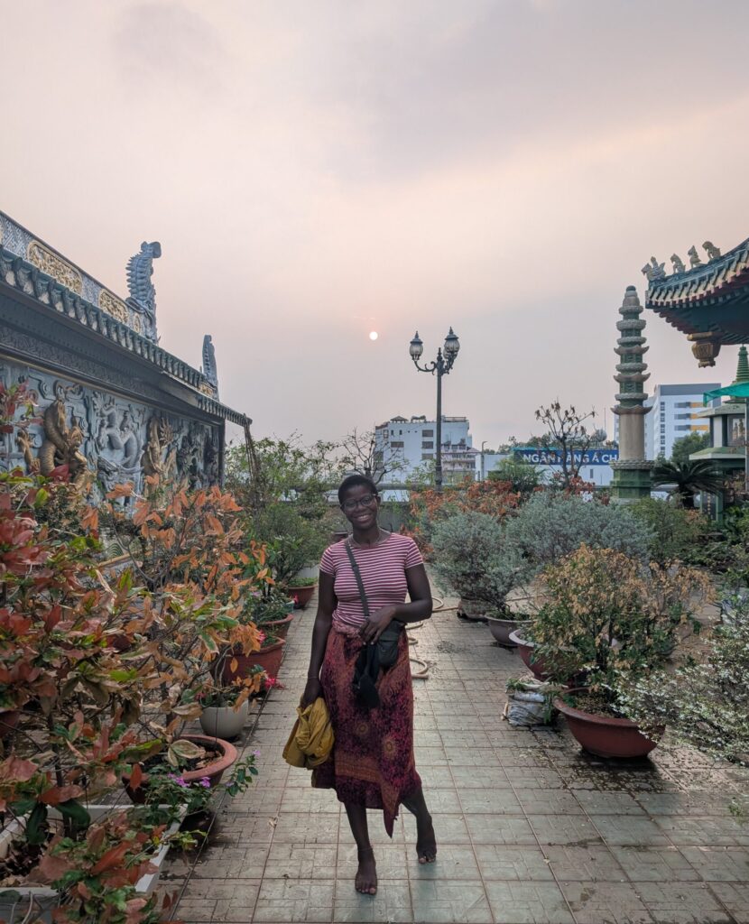 Mary-Ann standing on a roof-top temple garden, with a hazey sun in the background.