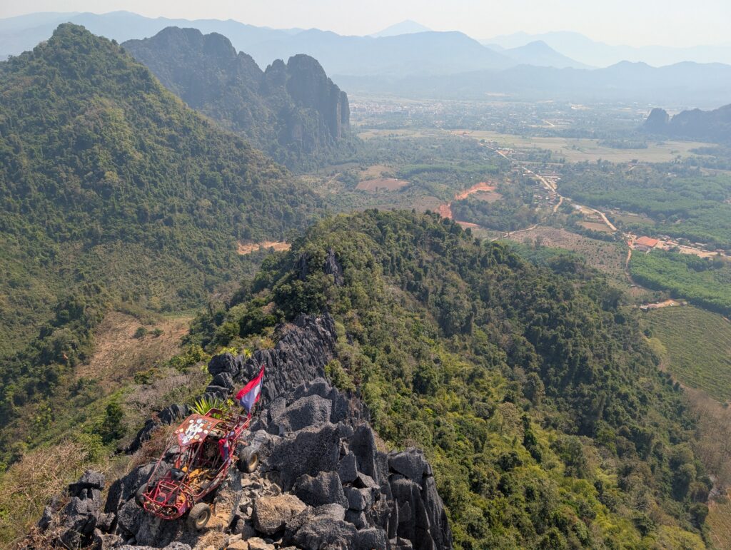 A rocky mountaintop view, including a dune buggy that has been put on display on a high peak.