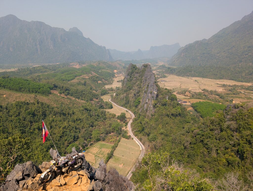 A hazy mountain top view, inclusing a motorbike mounted on a high peak.