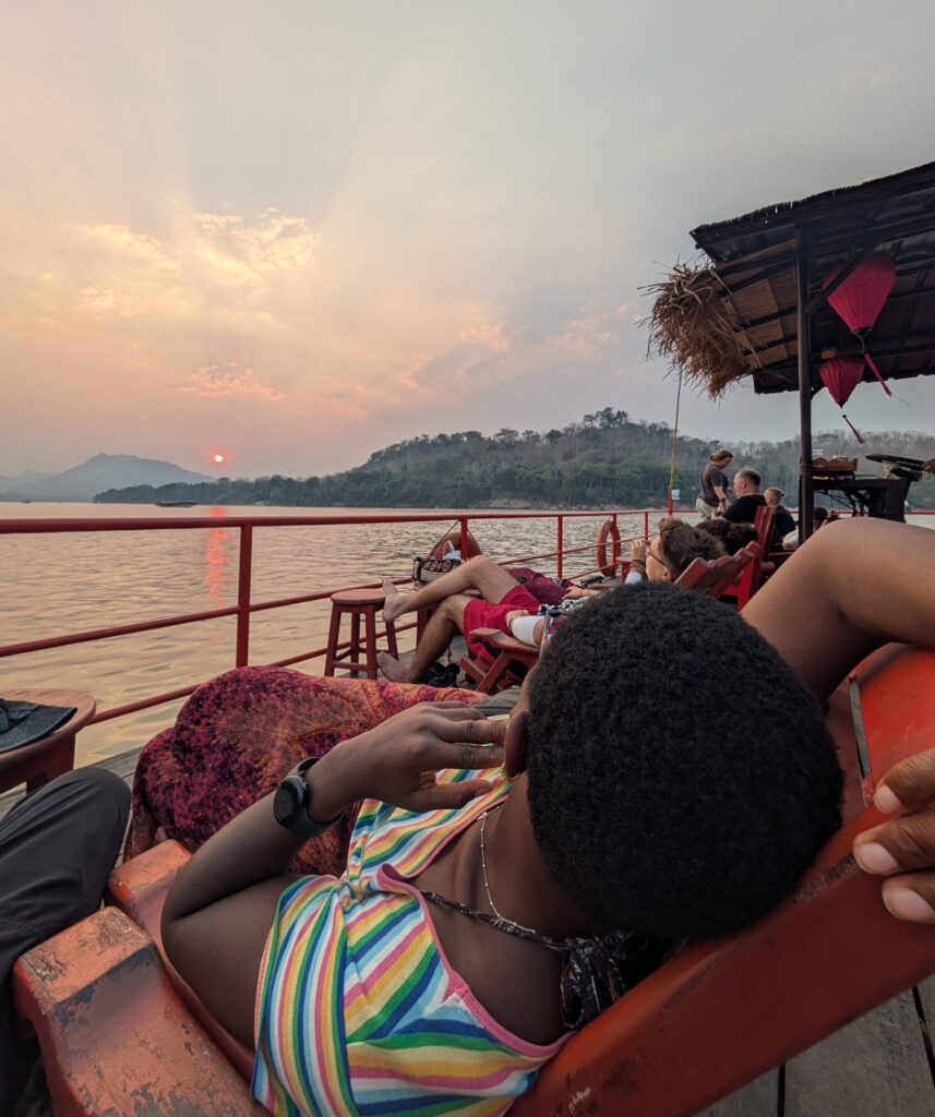 Mary-Ann lazing on a lounger infornt of an orange sunset, upon the river cruise boat.