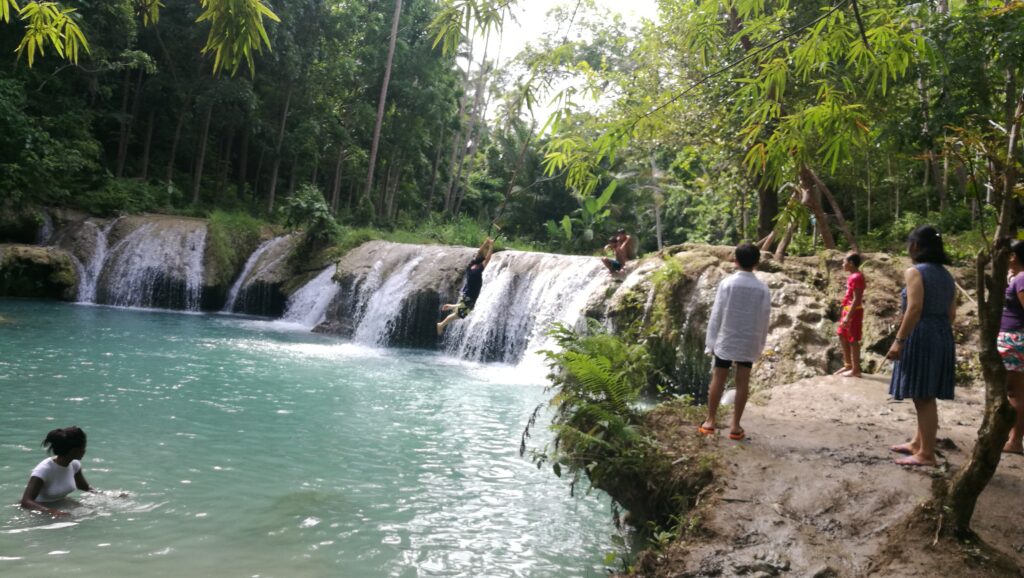 Mary-Ann watching a local use a rope swing to jump into the blue water of a waterfall pool on Siquijor.