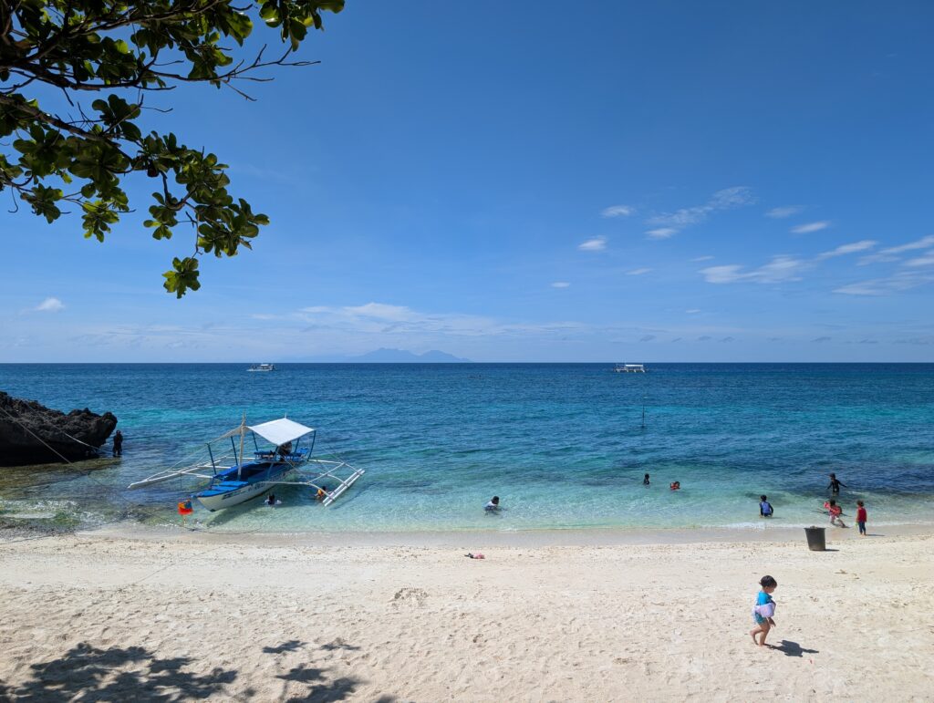 A daytime photo of a lovely local beach in Anda, with some dive boats out to see.