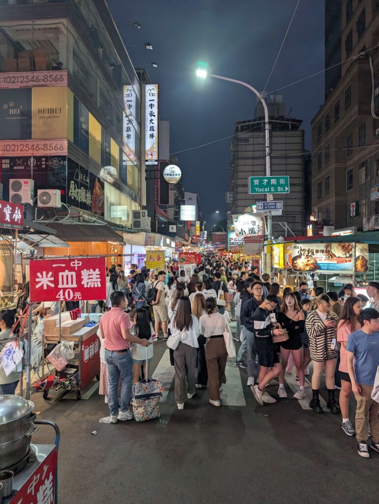 A shot of the buy Taichung night food market. Bustling with lights, food stalls and people.