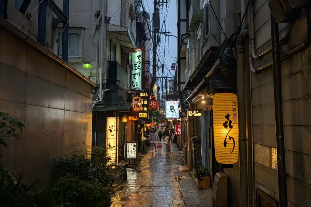 An image of a wet and rainy back alley in Osaka, lined with lanterns.
