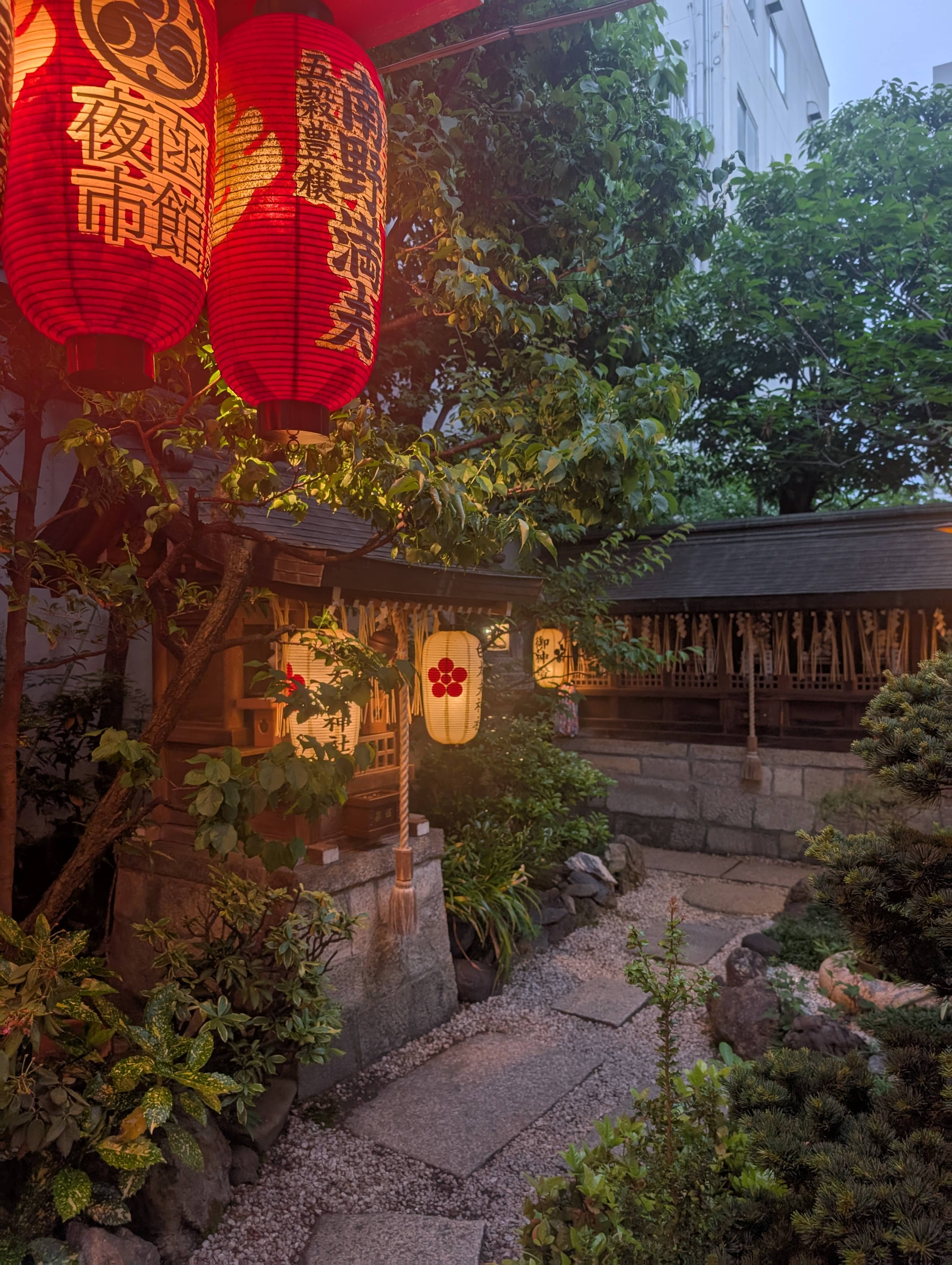 A dusky image of a small back alley shrine, lit up byt lanterns,