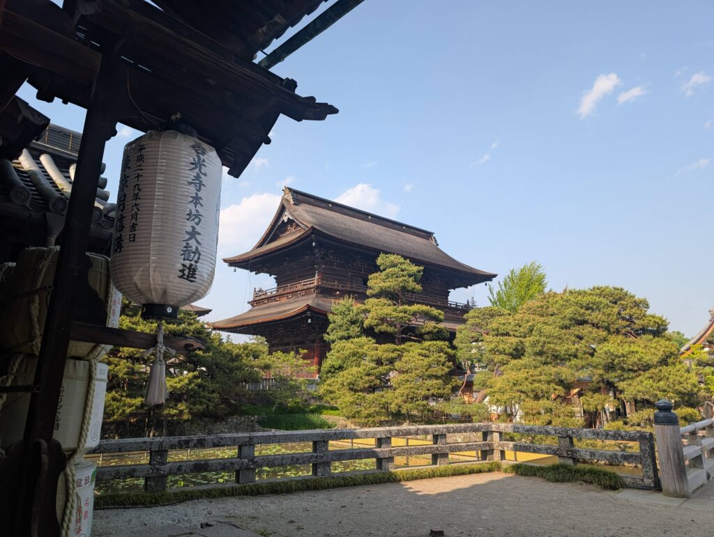 An image if a temple, behind some well pruned trees, and a lantern in the foreground.