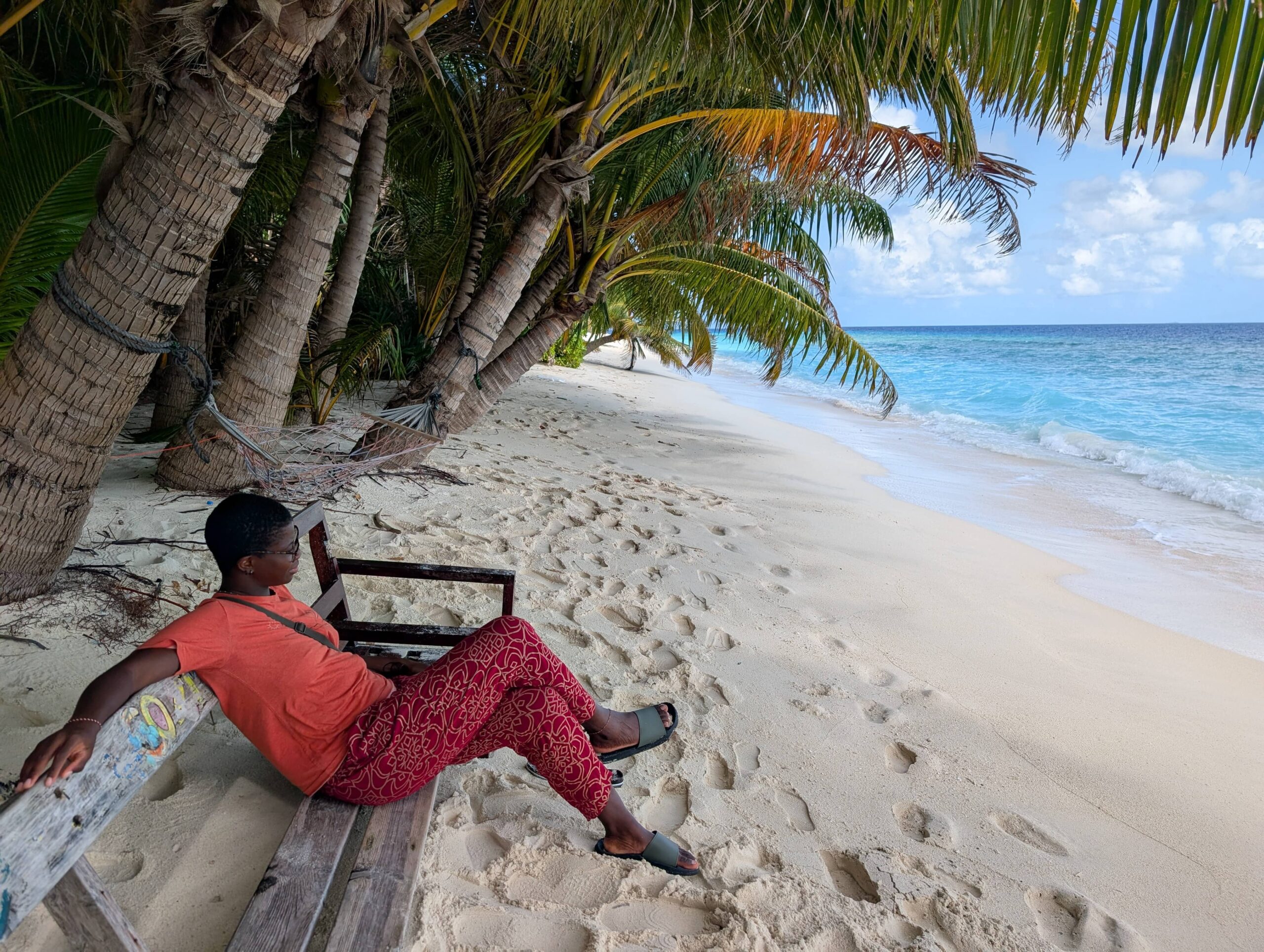 Mary-Ann sitting on a bench on the beach, under palm trees.
