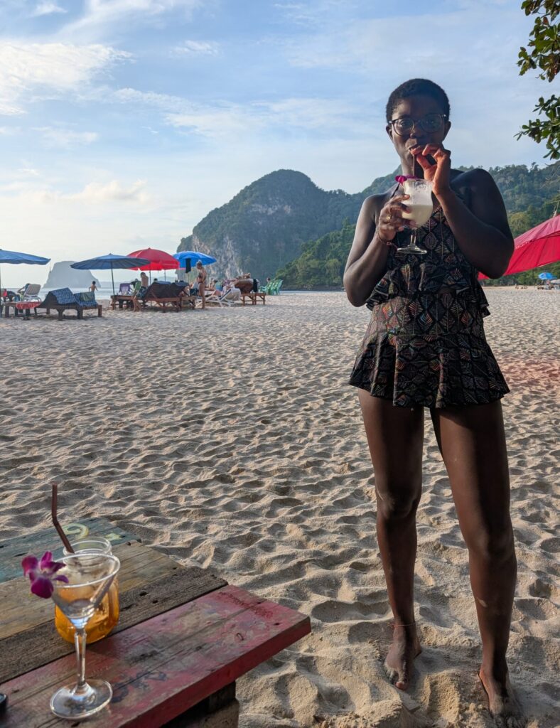 Mary-Ann drinking a cocktail on a beach somewhere in Thailand.
